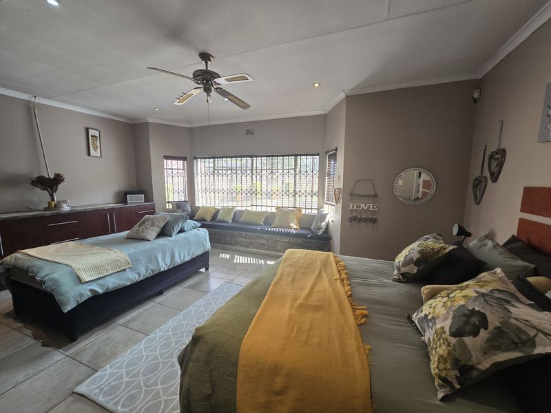 Spacious bedroom featuring tiled flooring, built-in cabinetry, a ceiling fan, and a large window with security bars and a built-in bench seat.