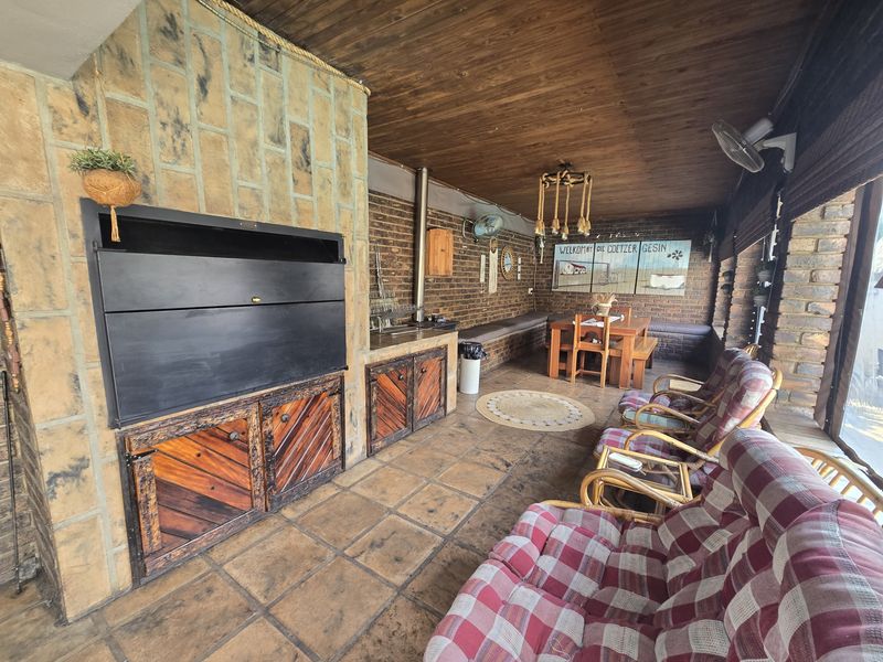 Covered patio area featuring a built-in braai, stone-clad fireplace, brick walls, timber ceiling, and built-in bench seating, ideal for outdoor entertaining.