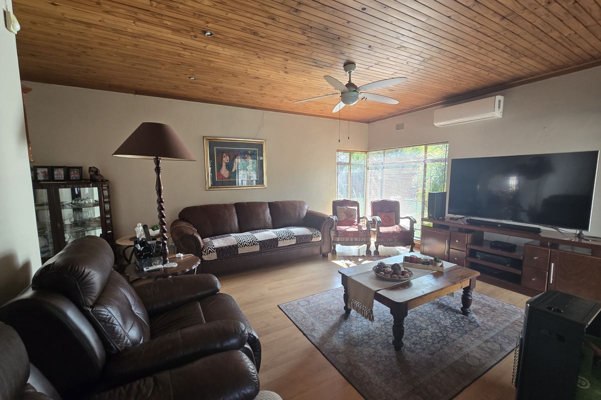 A comfortable living room featuring a warm timber-paneled ceiling, laminate flooring, and a split-system air conditioner for climate control.