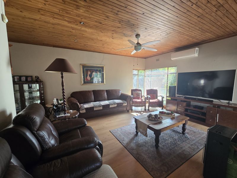 A comfortable living room featuring a warm timber-paneled ceiling, laminate flooring, and a split-system air conditioner for climate control.