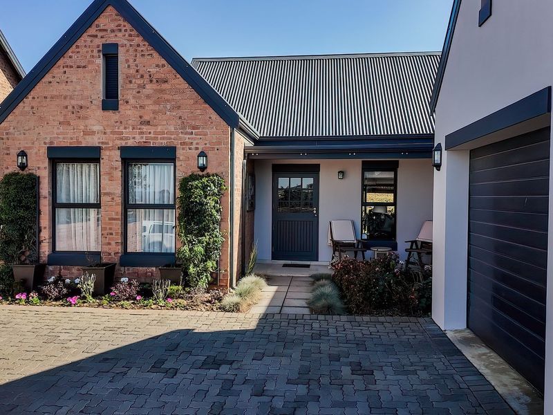 A well-maintained front facade featuring a combination of brick and rendered walls, a corrugated metal roof, paved driveway, and integrated garage.