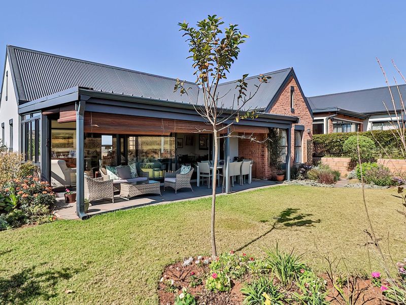A well-maintained rear exterior featuring a covered patio, brick and metal roof construction, and a landscaped garden area.
