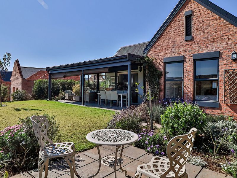 A well-maintained rear exterior view featuring an exposed brick facade, a covered patio area, and a landscaped garden with paved terrace.
