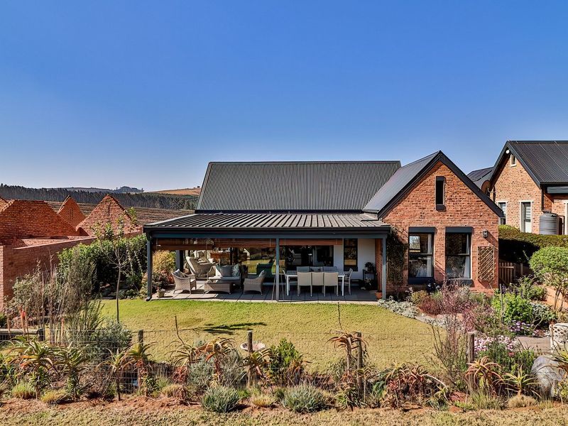 Rear view of a charming brick house featuring a covered patio, well-maintained garden, and modern corrugated metal roofing.