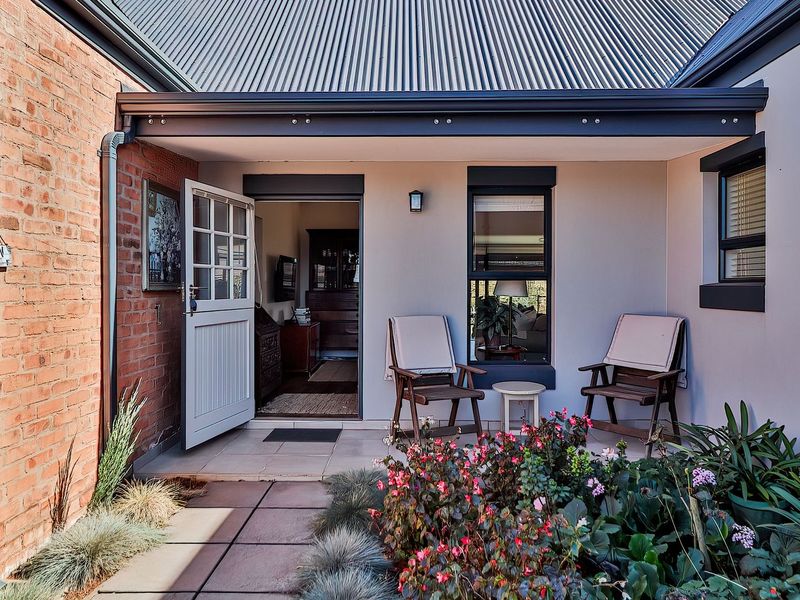 A charming covered patio area featuring exposed brickwork, tiled flooring, and a corrugated metal roof, providing a welcoming entrance to the home.