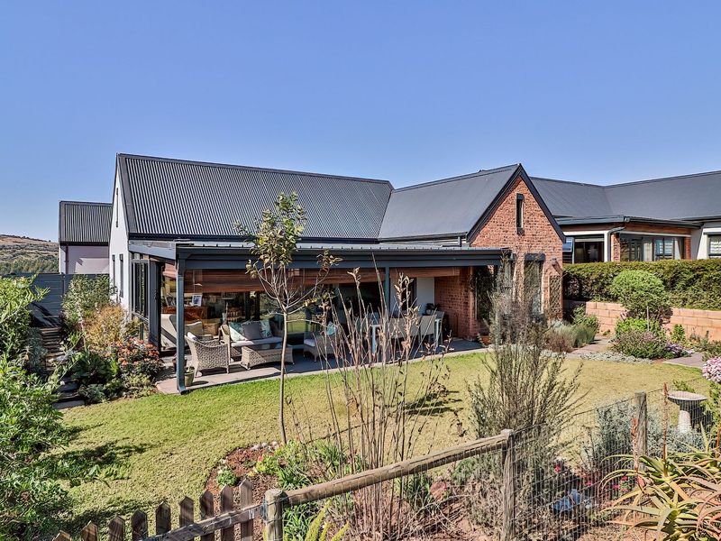 Rear view of the property featuring a covered patio, brick and metal roof construction, and a well-maintained landscaped garden.
