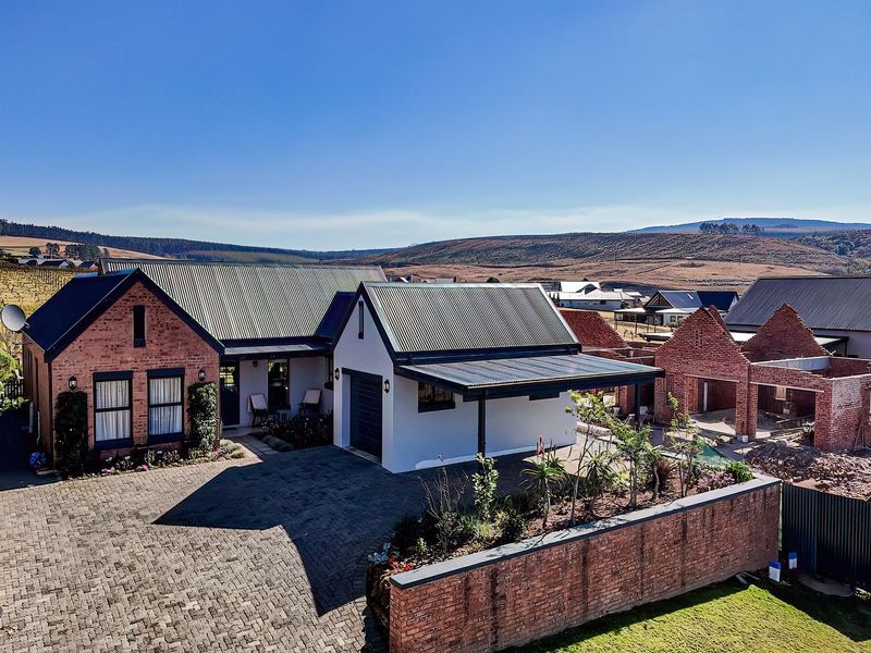 Aerial view of a brick-faced residence featuring a paved driveway, garage, and covered carport, situated in a scenic rural estate setting.