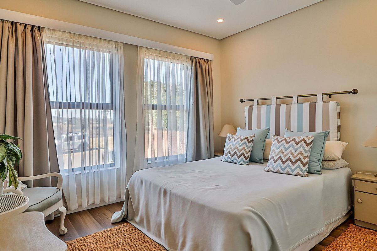 A well-maintained bedroom featuring laminate flooring, recessed downlighting, and large windows with integrated curtain tracks.