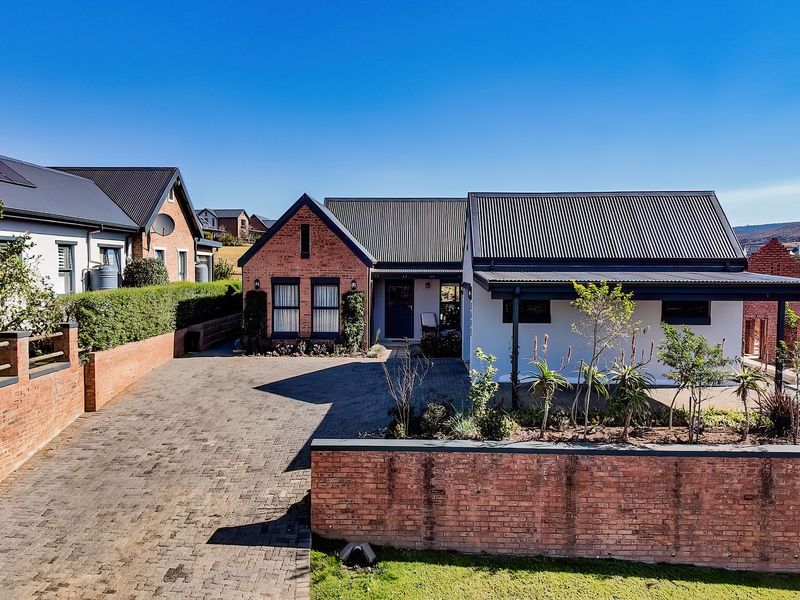 A well-maintained modern brick home featuring a paved driveway, covered patio area, and corrugated metal roofing in a neat residential setting.
