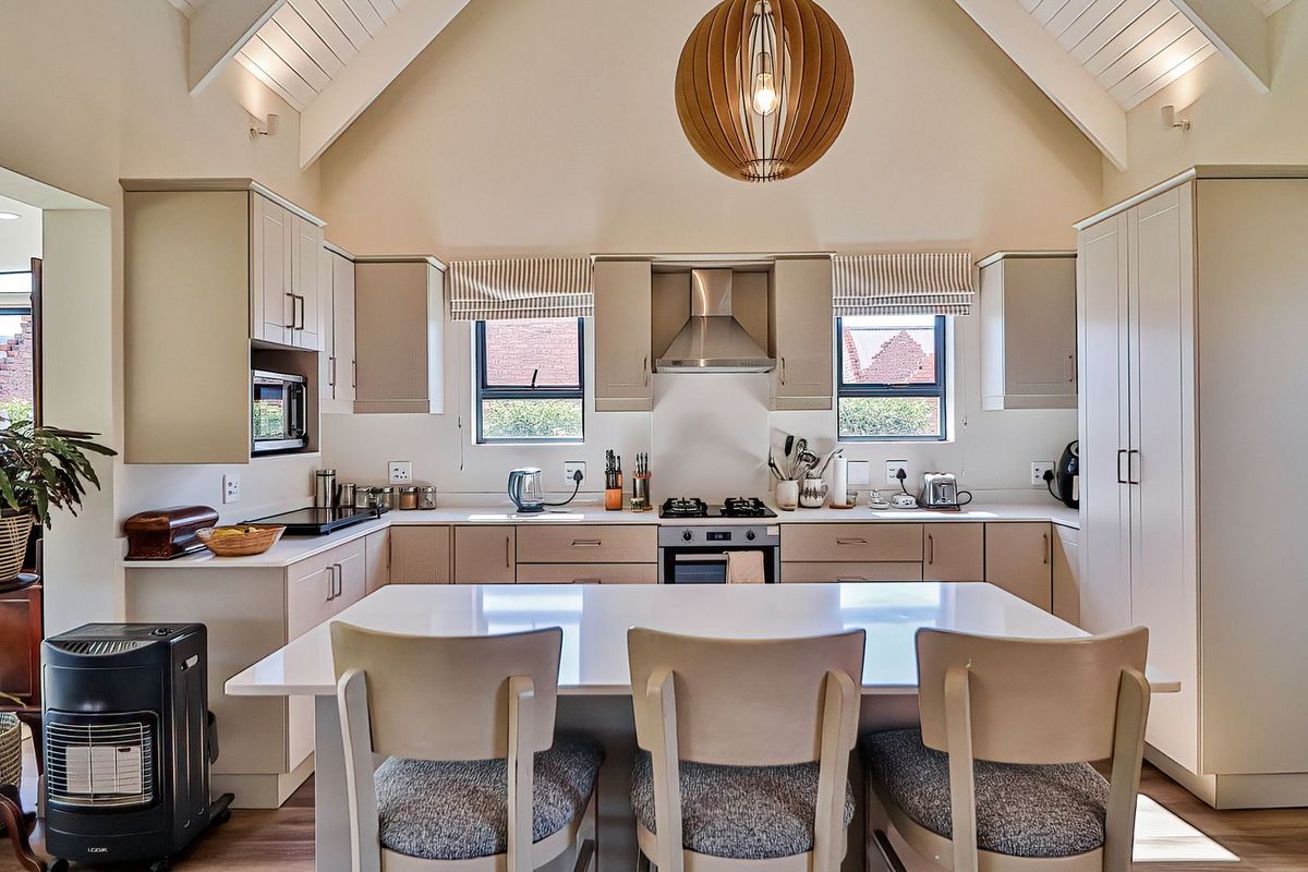 Modern kitchen featuring a central island, vaulted ceilings, neutral cabinetry, and integrated appliances, offering a bright and functional culinary space.