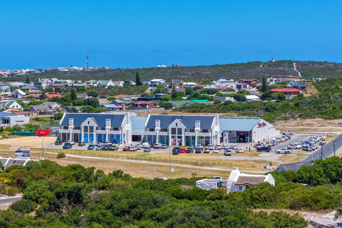 An aerial view of a commercial retail complex with a large parking area, situated within a coastal residential neighborhood.