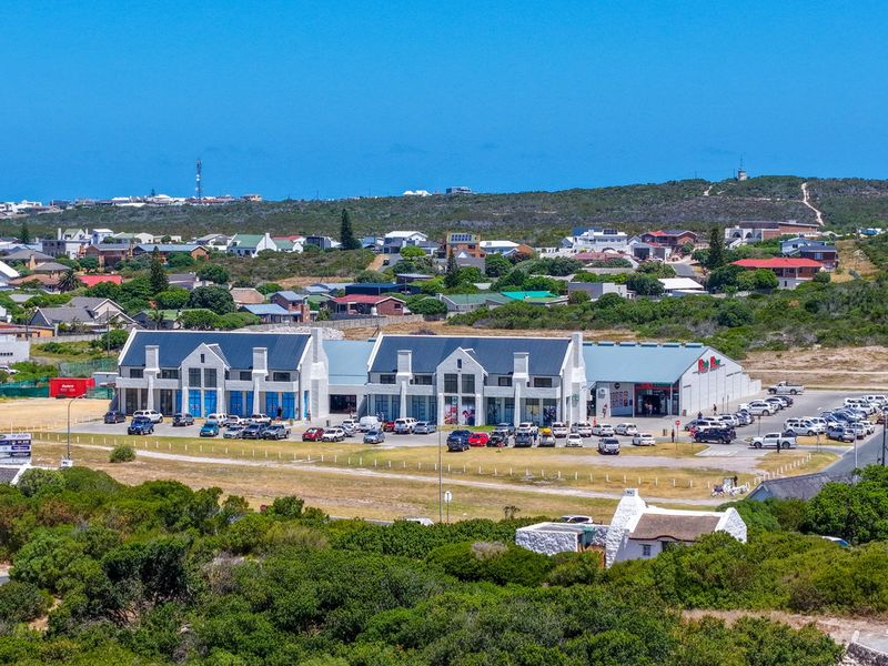 An aerial view of a commercial retail complex with a large parking area, situated within a coastal residential neighborhood.