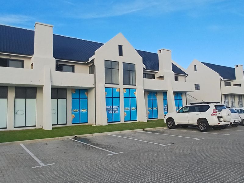Front elevation of a modern apartment complex featuring gabled roof architecture, white exterior walls, and a paved parking area.
