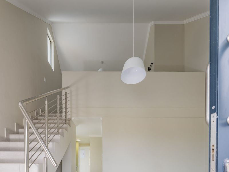 A bright and airy entrance hall featuring a modern staircase with stainless steel balustrades and a high vaulted ceiling.
