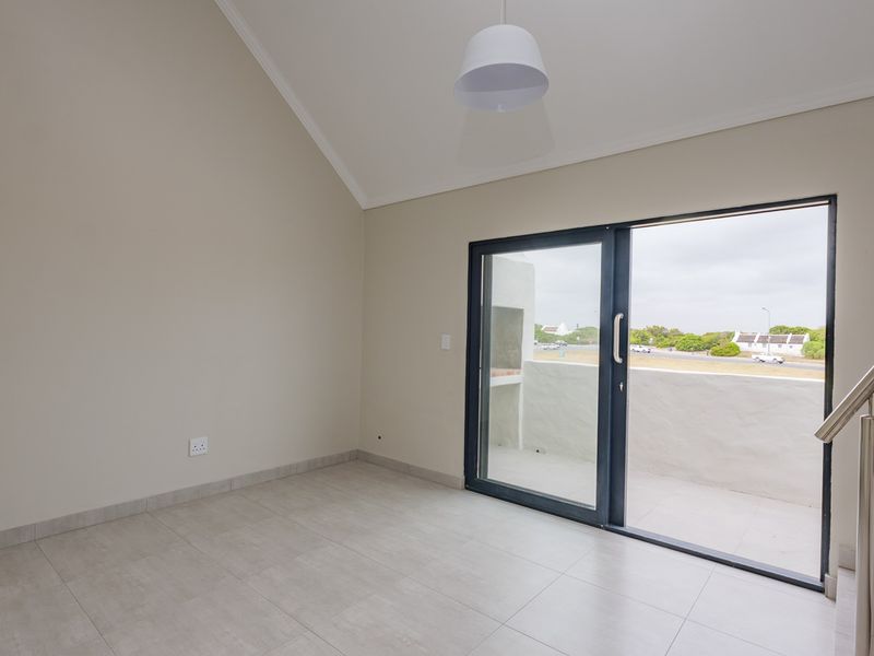 Bright and spacious living area featuring vaulted ceilings, modern tiled flooring, and a large sliding glass door leading to an outdoor balcony.