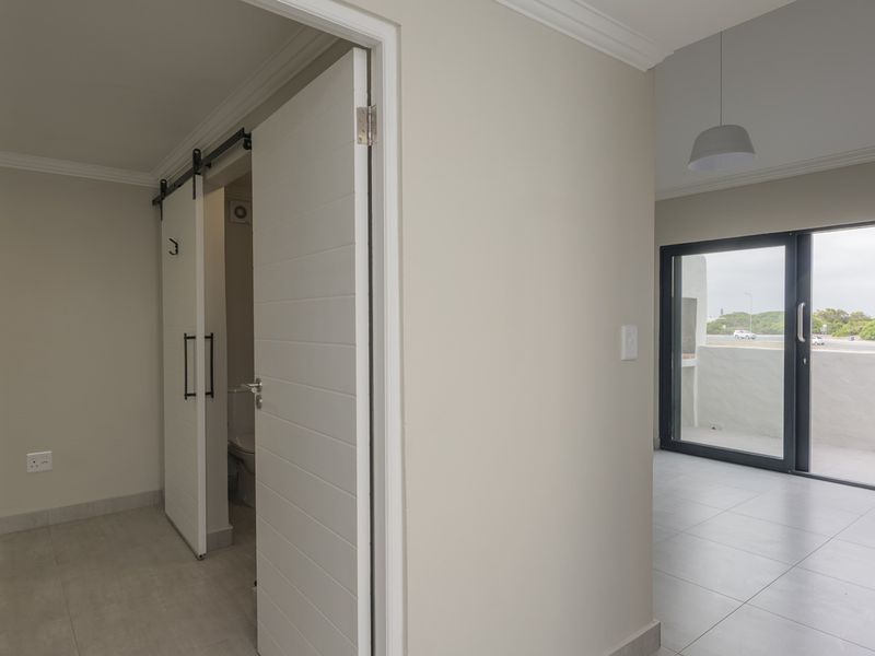 A bright, neutral hallway featuring tiled floors, crown molding, and a sliding barn door leading to an adjacent room with balcony access.