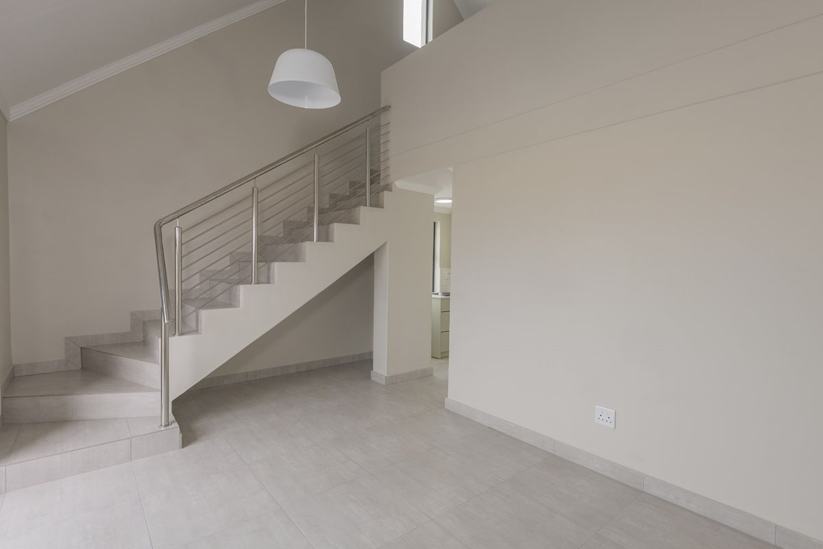 Spacious open-plan living area featuring a modern staircase with stainless steel balustrades, neutral tiled flooring, and high vaulted ceilings.