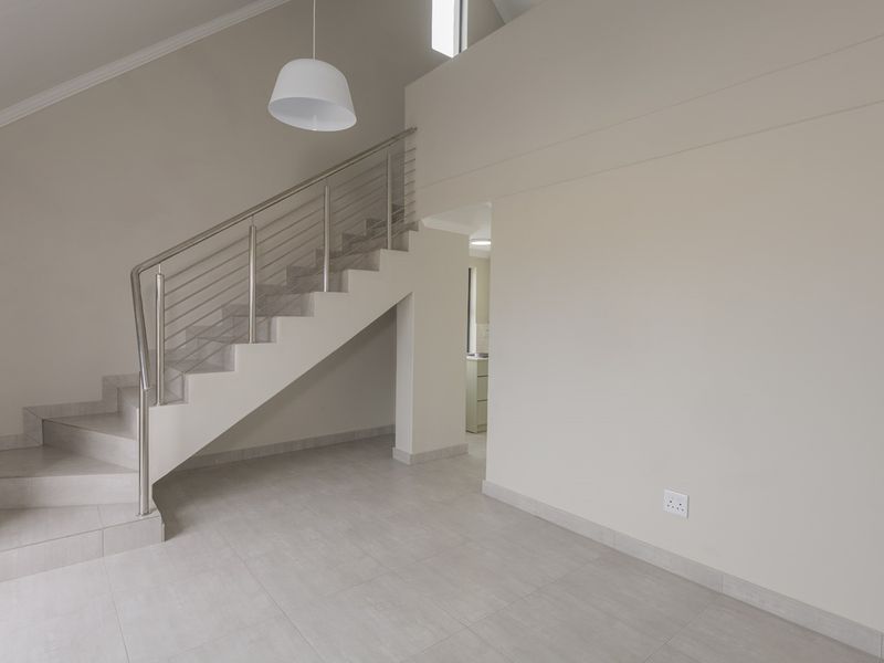 Spacious open-plan living area featuring a modern staircase with stainless steel balustrades, neutral tiled flooring, and high vaulted ceilings.