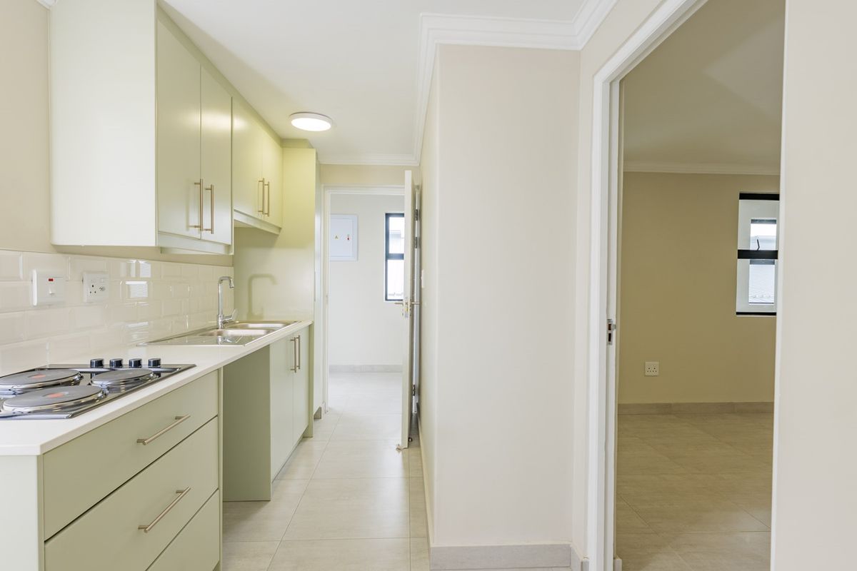 A clean, modern kitchen featuring light green cabinetry, a gas hob, subway tile backsplash, and tiled flooring, leading into an adjacent living area.