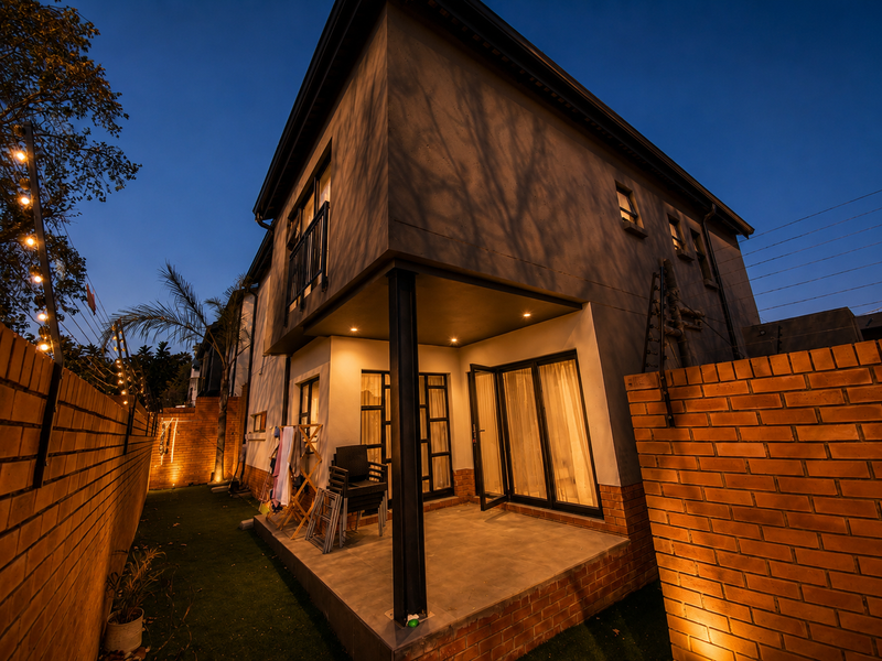 A modern townhouse rear elevation featuring a covered patio, brick boundary walls with electric fencing, and integrated outdoor lighting at dusk.