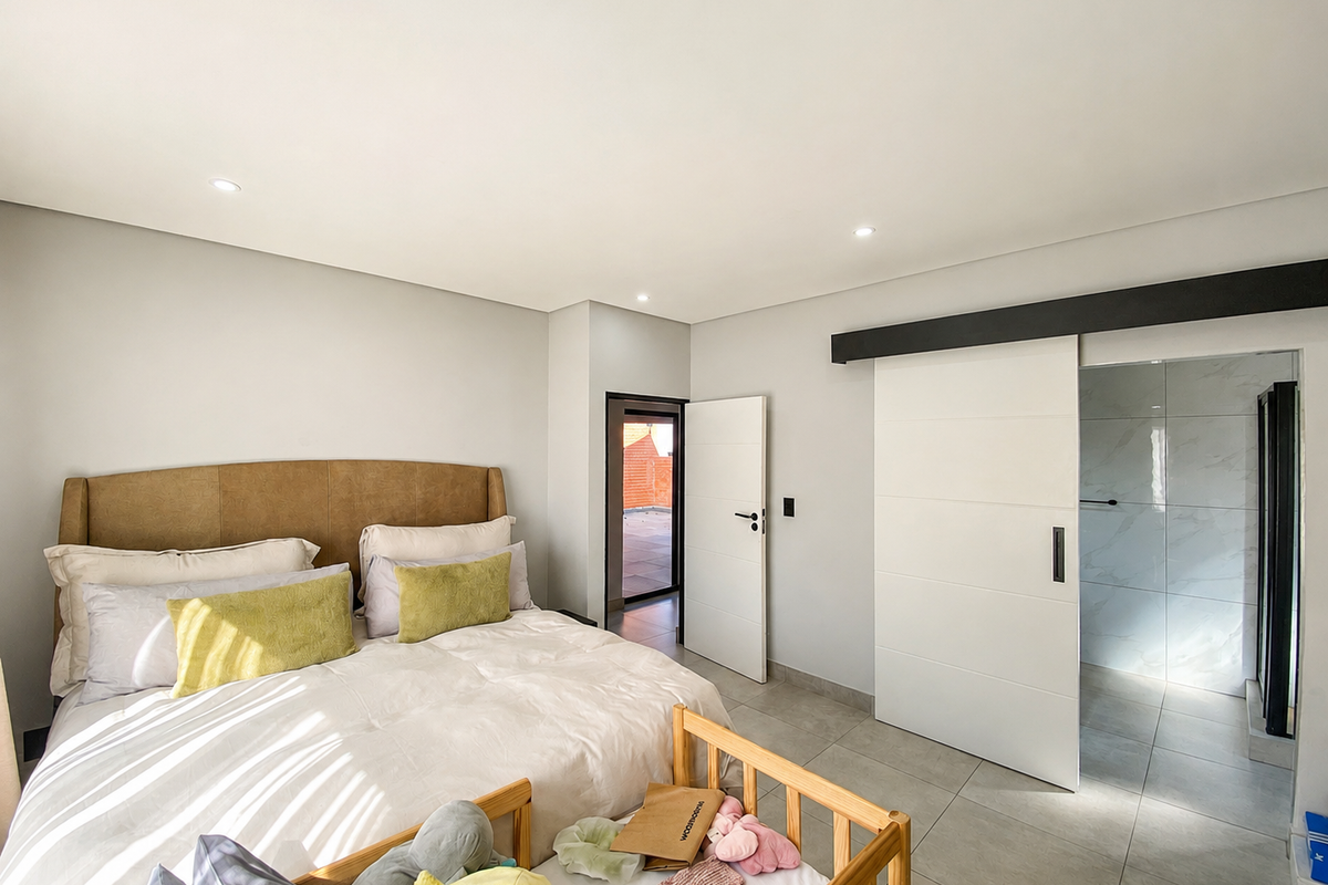Spacious bedroom featuring modern tiled flooring, recessed downlighting, and a sleek sliding barn door providing access to an en-suite bathroom.