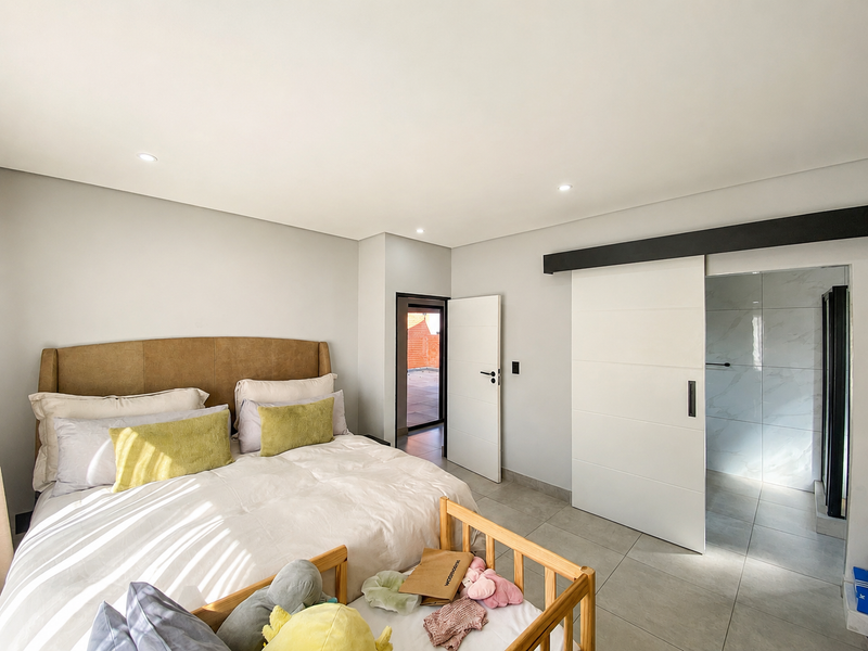 Spacious bedroom featuring modern tiled flooring, recessed downlighting, and a sleek sliding barn door providing access to an en-suite bathroom.