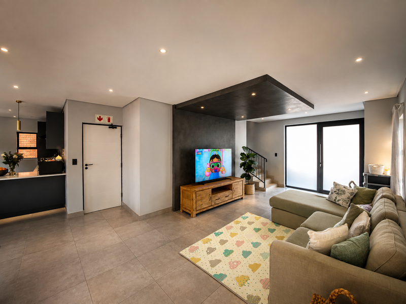 Modern open-plan living area featuring a sleek kitchen, tiled floors, a feature bulkhead ceiling, and direct access to the outdoors via sliding glass doors.