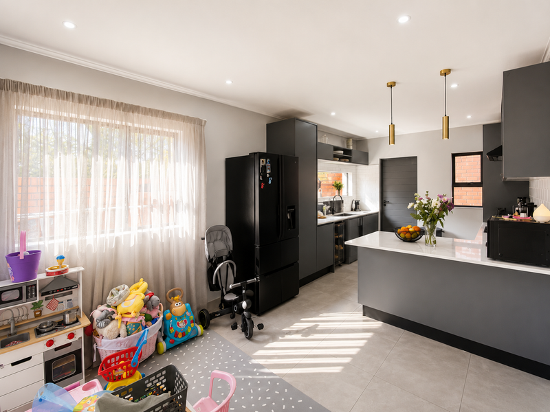 Modern open-plan kitchen featuring dark cabinetry, stone countertops, a central island, and contemporary pendant lighting, seamlessly integrated with the living area.