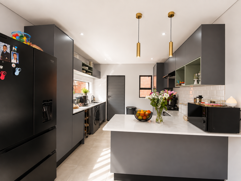 Modern kitchen featuring dark grey cabinetry, white quartz countertops, subway tile backsplash, and contemporary pendant lighting in a clean, well-maintained space.