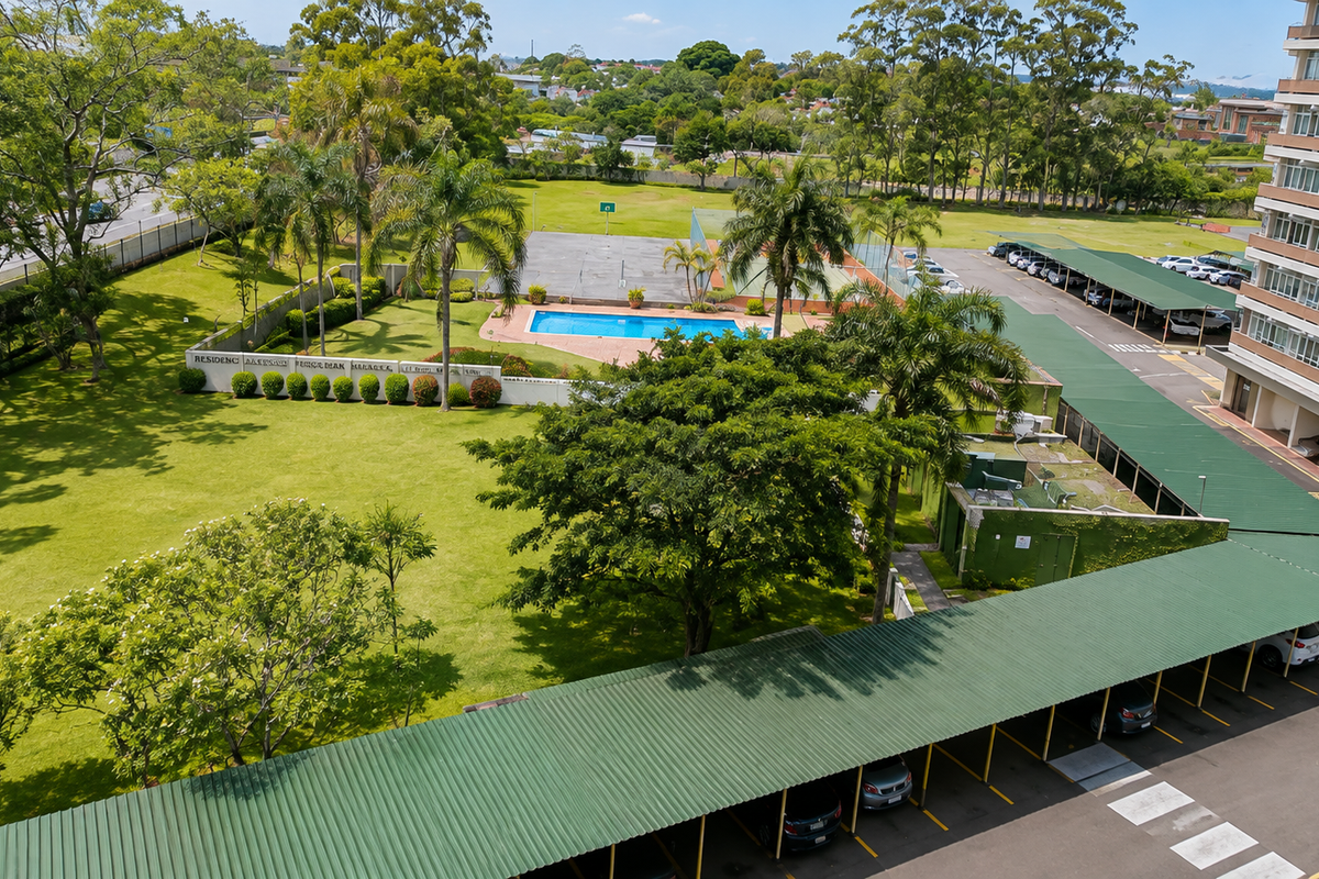 Aerial view of the apartment complex grounds featuring a swimming pool, tennis court, landscaped gardens, and extensive covered parking facilities.