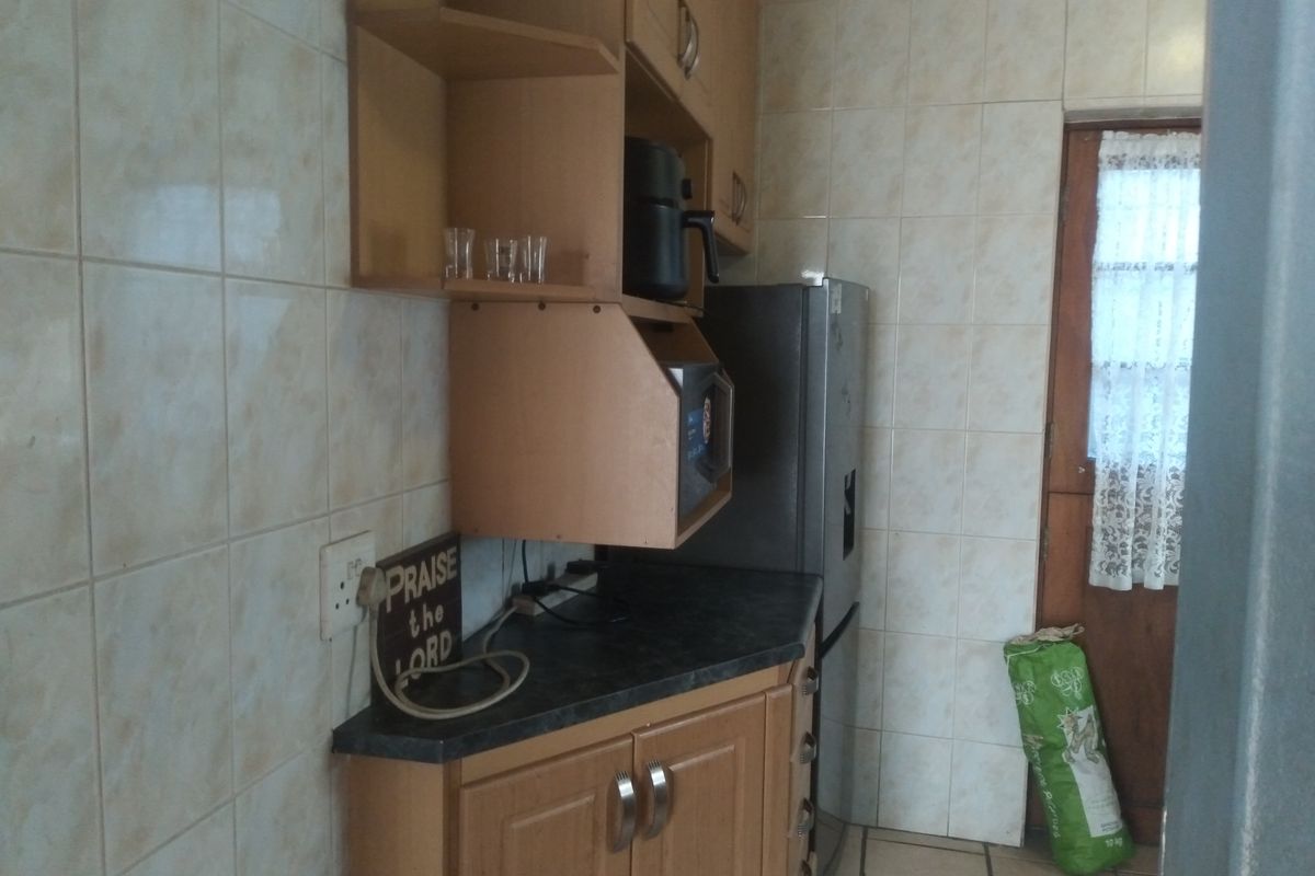 A compact kitchen area featuring laminate cabinetry, tiled walls, and tiled flooring, offering a functional layout with potential for modern updates.