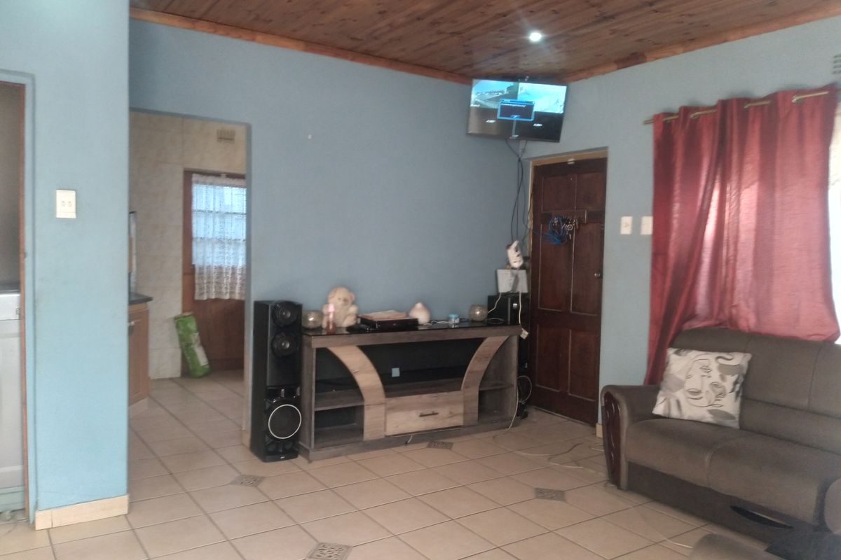 A living room featuring ceramic floor tiles and a timber ceiling, with an adjacent doorway leading to a secondary space.