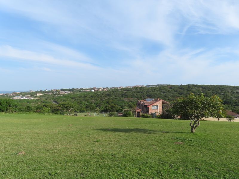 A wide-angle view of a grassy residential plot with surrounding coastal landscape and distant housing developments.