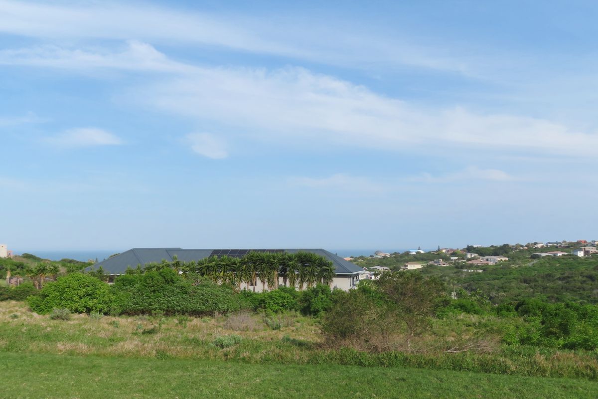 An elevated view of the residential property featuring a pitched roof with integrated solar panels, surrounded by natural landscape and coastal neighborhood views.