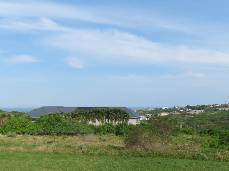 An elevated view of the residential property featuring a pitched roof with integrated solar panels, surrounded by natural landscape and coastal neighborhood views.