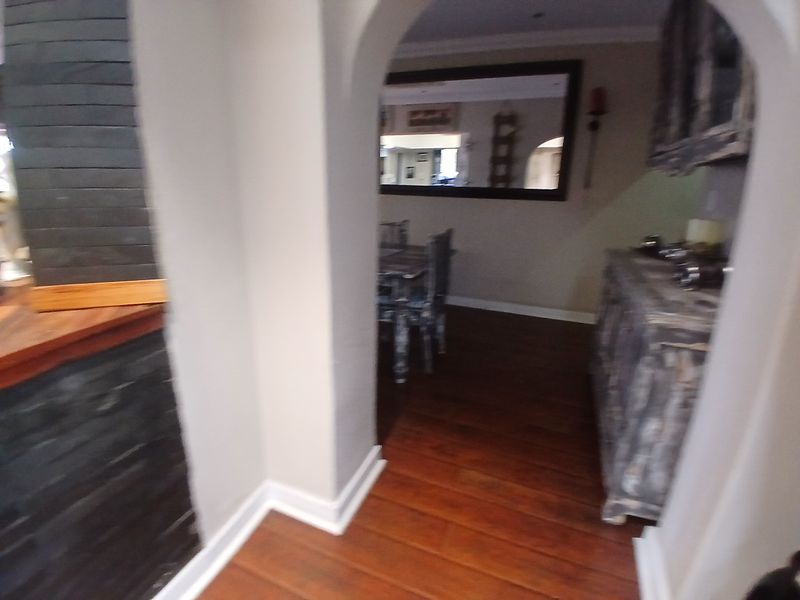 A transitional hallway space featuring an arched entryway, stone-clad pillar detail, and warm timber flooring leading into the adjacent living area.