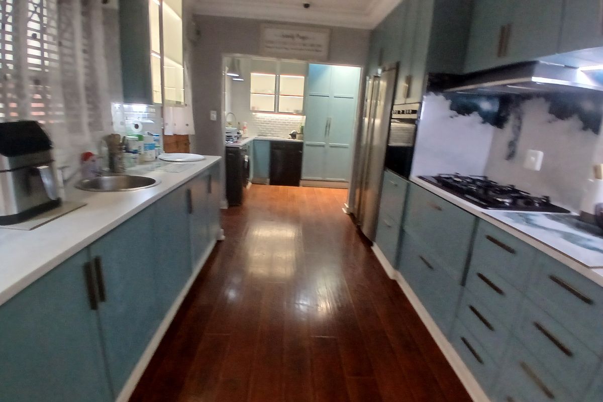 A well-appointed kitchen featuring blue cabinetry, stone countertops, a gas hob, built-in oven, and warm-toned laminate flooring with an adjacent scullery area.