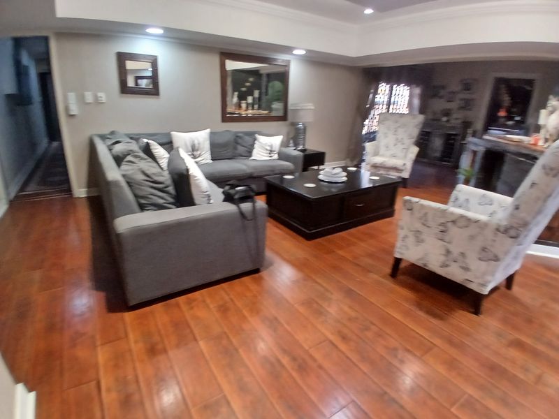 A spacious living room featuring warm-toned laminate flooring, recessed ceiling lighting, and elegant crown molding, creating a comfortable and inviting atmosphere.