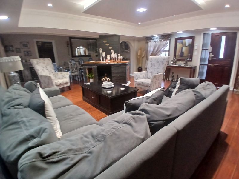 Spacious living room featuring hardwood flooring, a central stone-clad fireplace, and recessed ceiling lighting, creating a warm and inviting atmosphere.