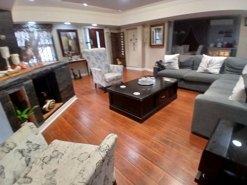 Spacious living room featuring warm hardwood flooring, recessed lighting, and a prominent stone-clad fireplace, creating a comfortable and inviting atmosphere.