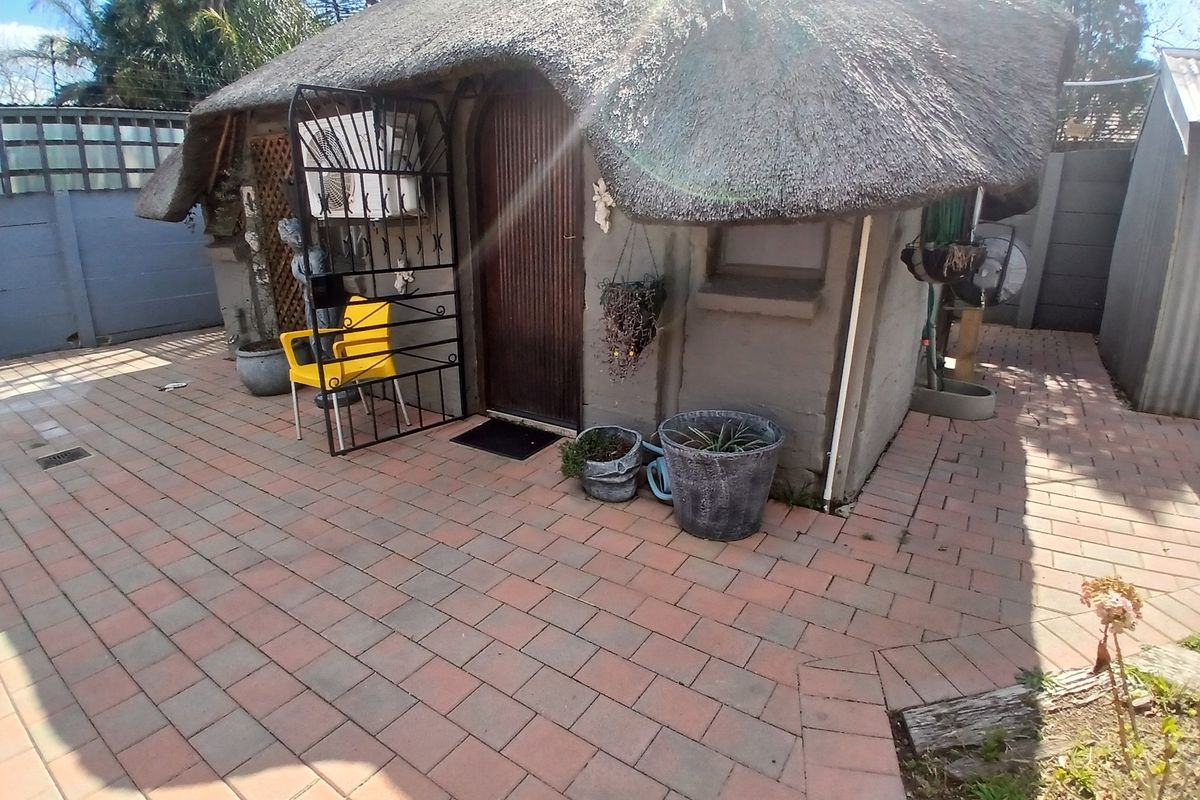 Rear exterior view of a small structure featuring a traditional thatch roof, paved patio area, and secure entrance gate.