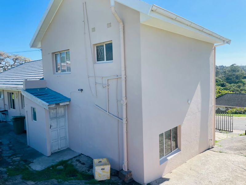 A side and rear view of the house showing the exterior wall, roofline, downpipes, and concrete driveway area.