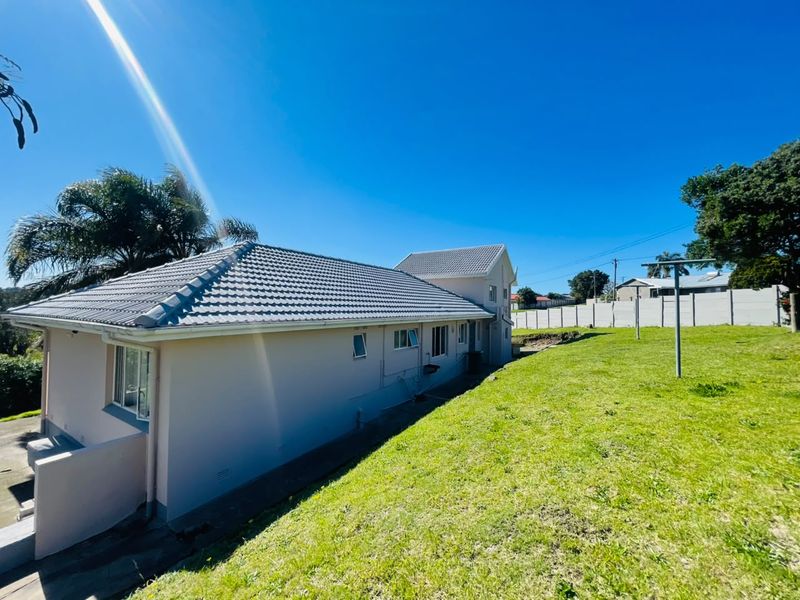 Rear view of the property showing the tiled roof, exterior walls, and a spacious grassed backyard with a boundary wall.