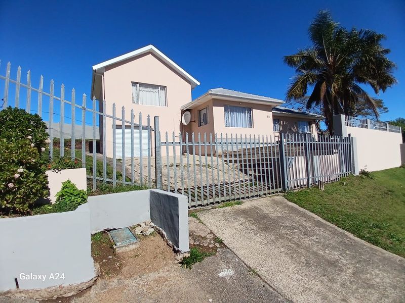 Front exterior view of a residential house featuring a concrete driveway, metal security fencing, and a perimeter wall.