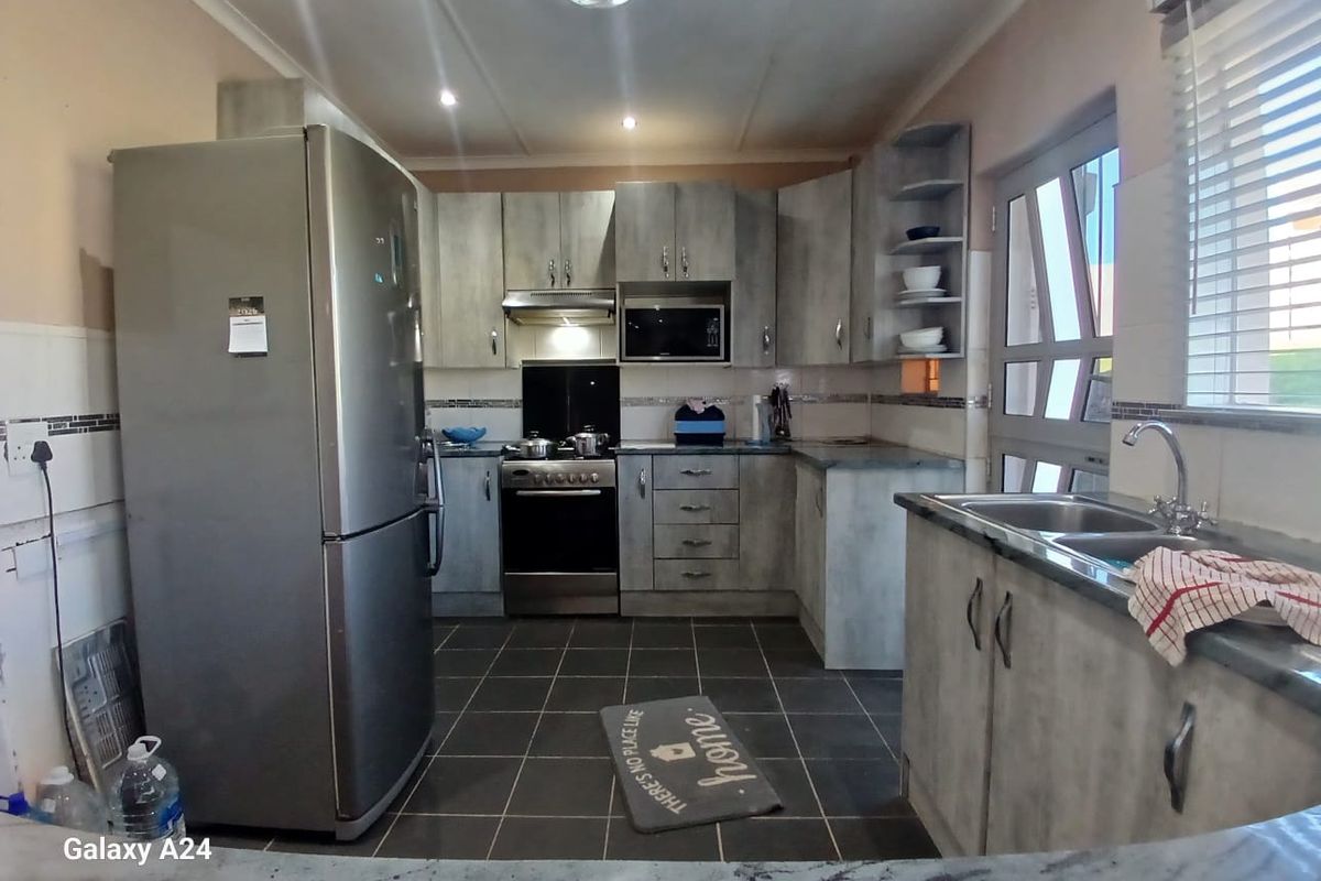 A functional kitchen featuring grey-toned cabinetry, a built-in oven with extractor, double basin sink, and tiled flooring with natural light from the side window.