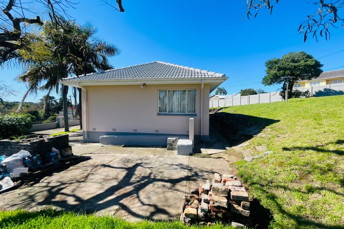 Rear view of the property featuring a concrete patio area, tiled roof, and surrounding garden space with established trees.