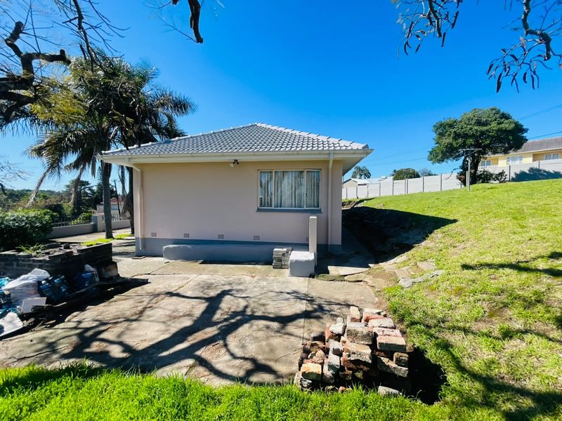 Rear view of the property featuring a concrete patio area, tiled roof, and surrounding garden space with established trees.
