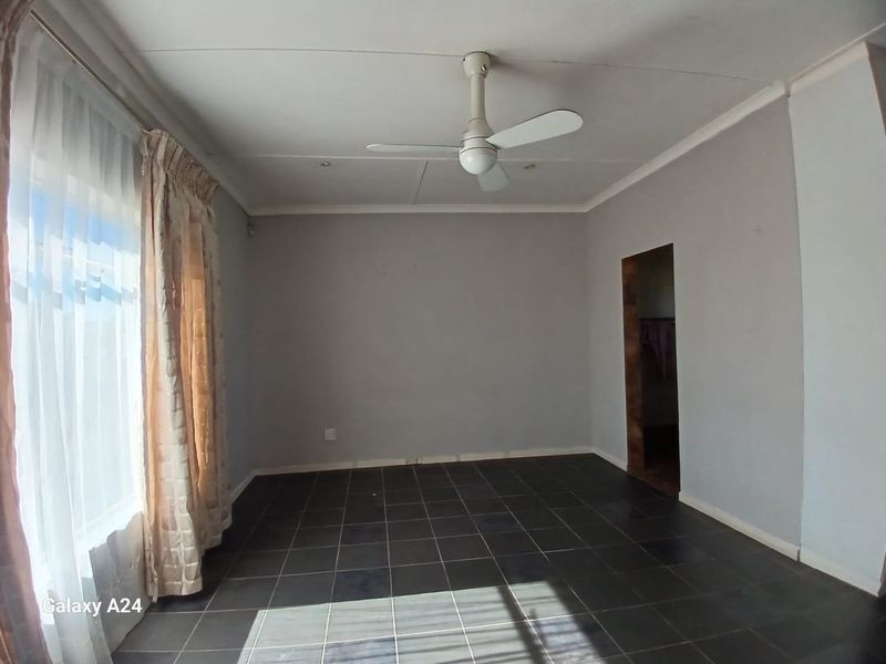 An empty living room featuring dark tiled flooring, a ceiling fan, and coved cornicing, awaiting personal touches to define the space.