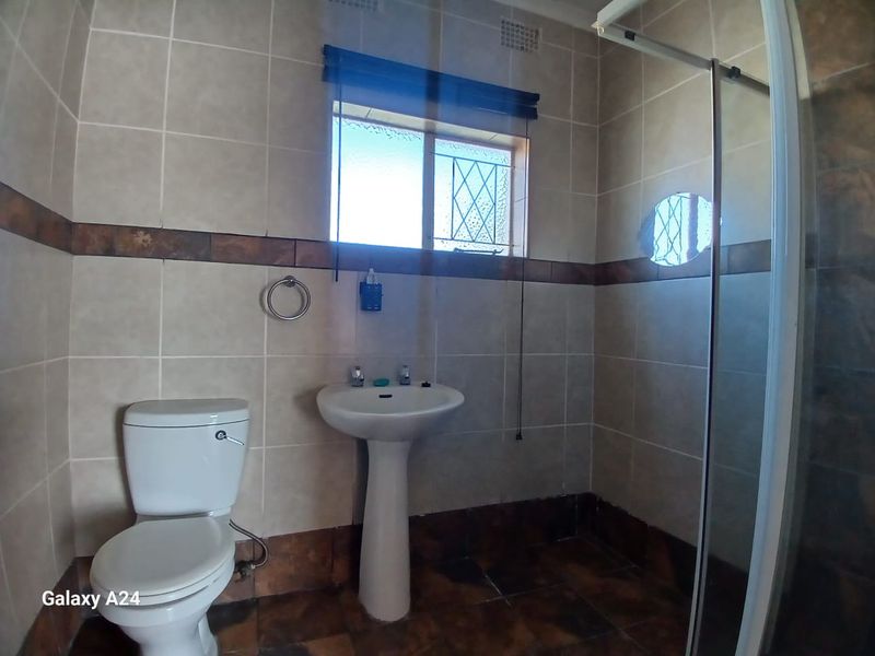 A functional bathroom featuring a pedestal basin, toilet, and a glass-enclosed shower with tiled walls and flooring.