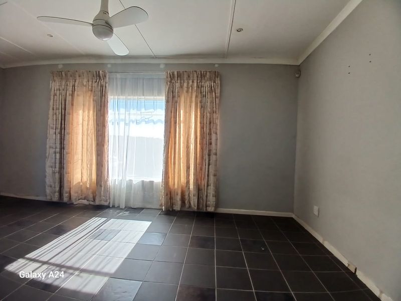An empty living room featuring dark tiled flooring, a ceiling fan, and recessed lighting, awaiting personal touches and minor cosmetic repairs.